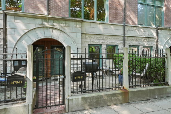 Front view of a multi-story building with brick and stone facade, gated entry, and patio area.