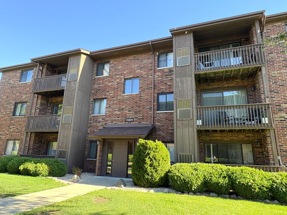 Front view of a three-story brick apartment building with balconies.