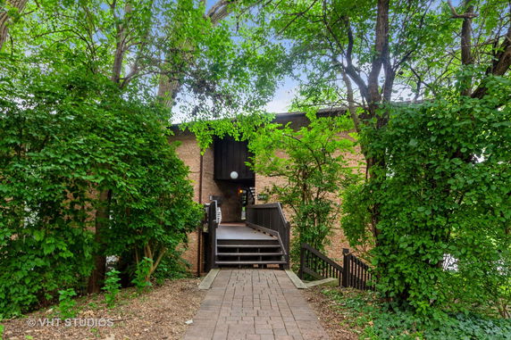 Front view of a brick building with a pathway leading to the entrance surrounded by trees.
