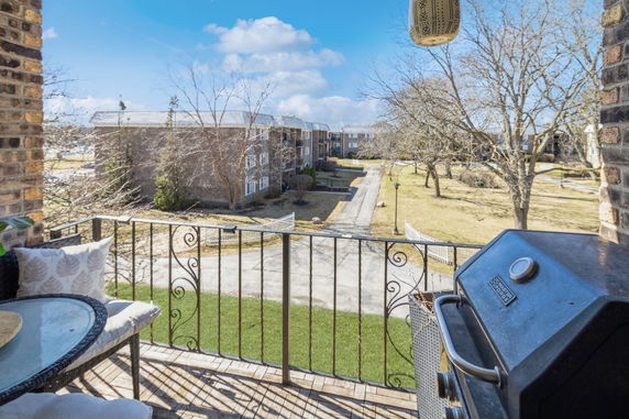View of a residential area with multiple apartment buildings, seen from a balcony with patio furniture and a grill.