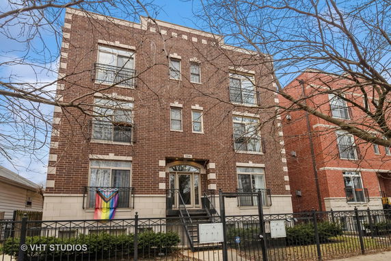 Front view of a three-story brick apartment building with multiple windows and a gated entrance.