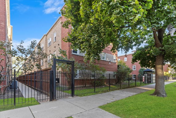 Front view of a multi-story brick building with a fenced entrance.