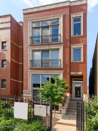 Front view of a three-story brick building with large windows and a small front yard.