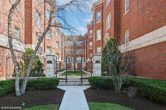 Front view of a red brick multi-story apartment building with gated entrance.
