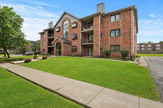 Front view of a three-story brick apartment building with balconies.