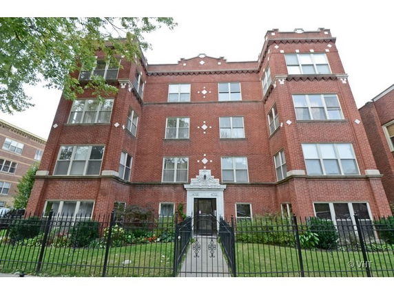 Front view of a multi-story brick apartment building with a gated entrance.