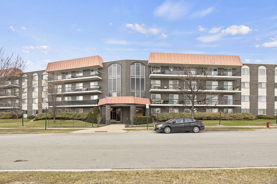 Front view of a multi-story apartment building with a reddish-brown roof and balconies.