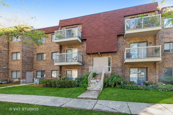 Front view of a multi-story brick apartment building with balconies and a central entrance.