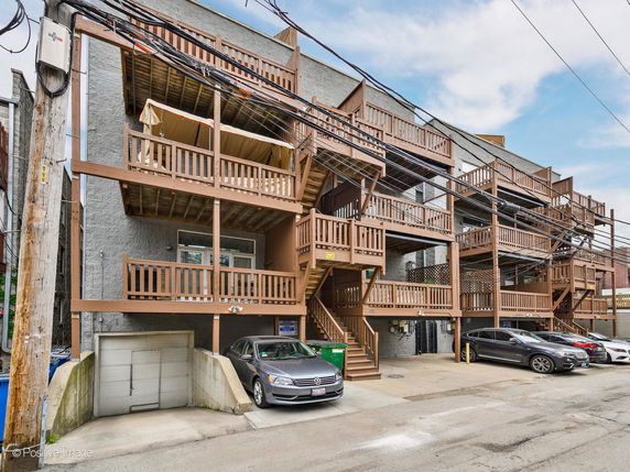 View of a multi-story building with wooden balconies and parking area.