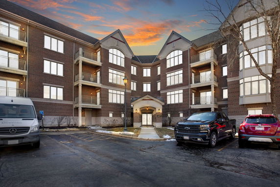 Front view of a multi-story brick building with balconies and parking area.