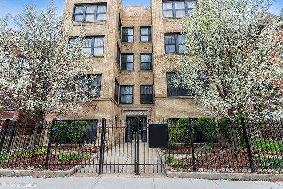 Front view of a multi-story brick apartment building with large windows and a gated entrance.