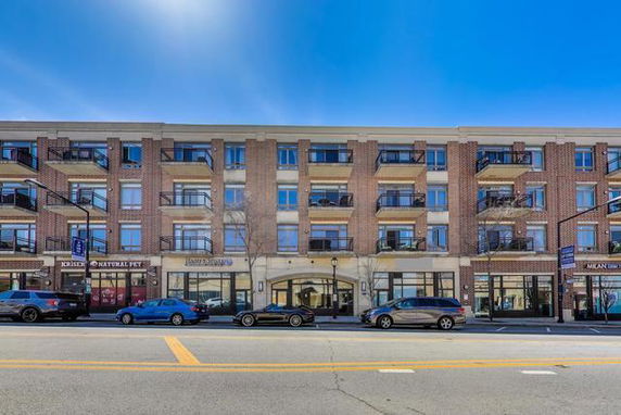Front view of a multi-story brick building with balconies and storefronts on the ground level.
