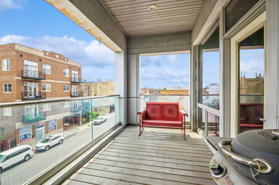 View from a balcony with glass railing overlooking adjacent buildings and a street.