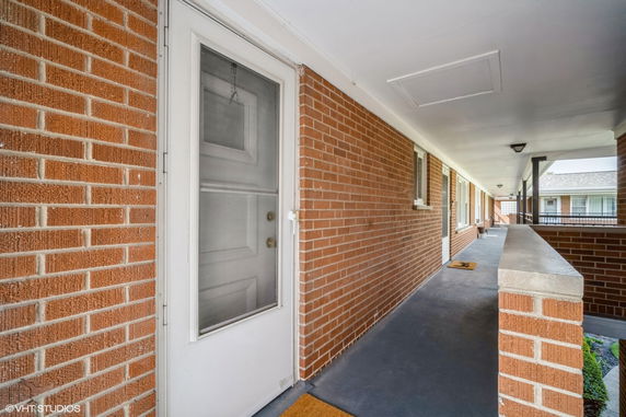 View of a brick exterior corridor with doors and a railing.
