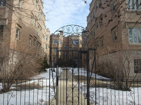 Front view of a multi-story brick building with decorative metal archway and gated entrance.