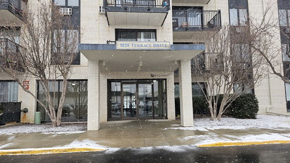 Front view of a multi-story building with balconies and glass entrance door.