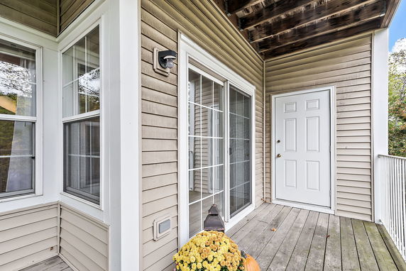 Exterior view of a house with sliding glass door and white entrance door on a wooden deck.
