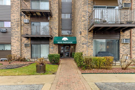 Front view of a brick apartment building with balconies and entryway.