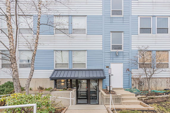 Front view of a multi-story building with blue and white siding and a metal awning over the entrance.