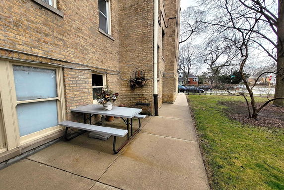 Front view of a brick building with multiple windows and a picnic table on the pavement.