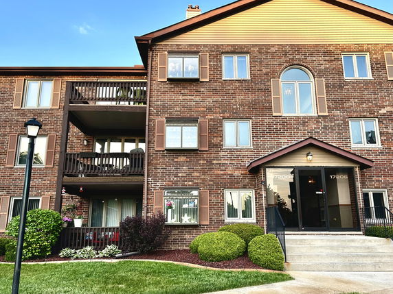 Front view of a multi-story brick apartment building with balconies and a gabled entrance.