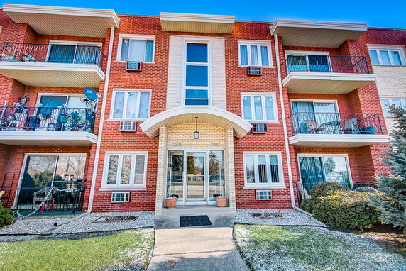 Front view of a three-story brick apartment building with balconies.