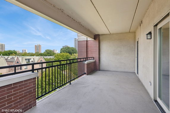 Outdoor balcony with metal railing overlooking buildings and greenery.