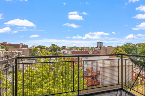 View from a balcony overlooking a cityscape with trees and buildings under a clear blue sky.