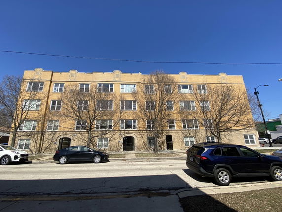 Front view of a four-story apartment building with yellow brick exterior.
