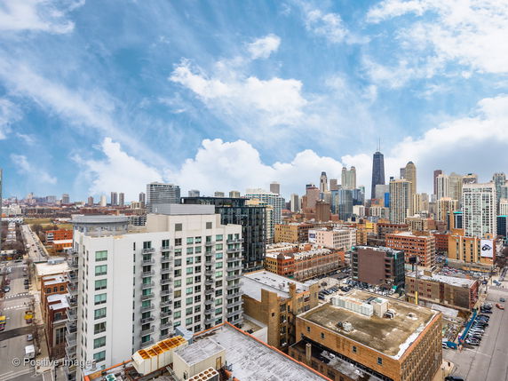 Panoramic cityscape view showing multiple high-rise buildings under a partly cloudy sky.
