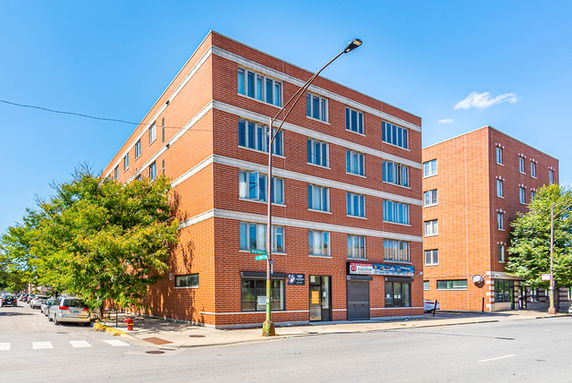 Front and side view of a multi-story brick building on a street corner.