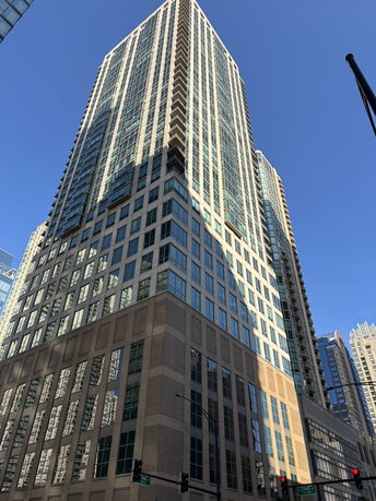 Front view of a tall modern skyscraper with glass windows against a clear blue sky.