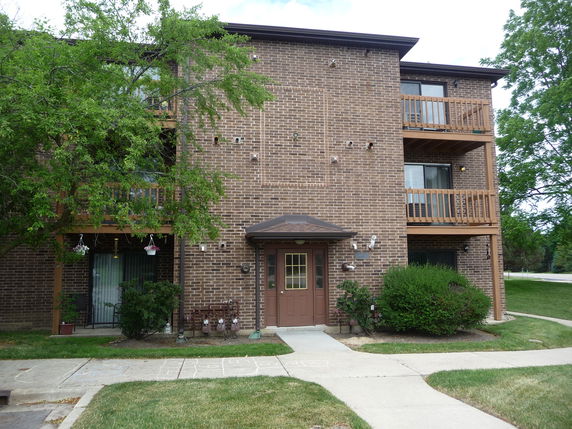 Front view of a three-story brick apartment building with balconies.