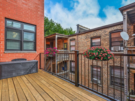 View from a rooftop deck with wooden flooring and railing, overlooking adjacent brick buildings.