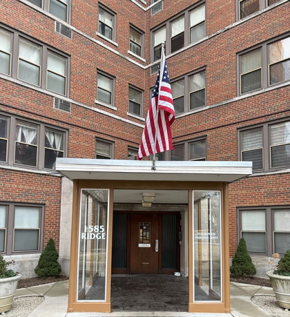 Front view of a multi-story brick building with an entrance canopy and American flag.