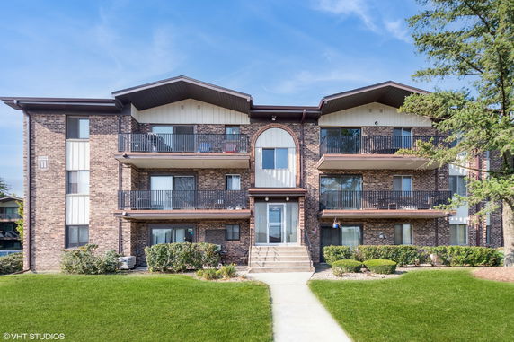 Front view of a brick apartment building with balconies and entrance stairs.