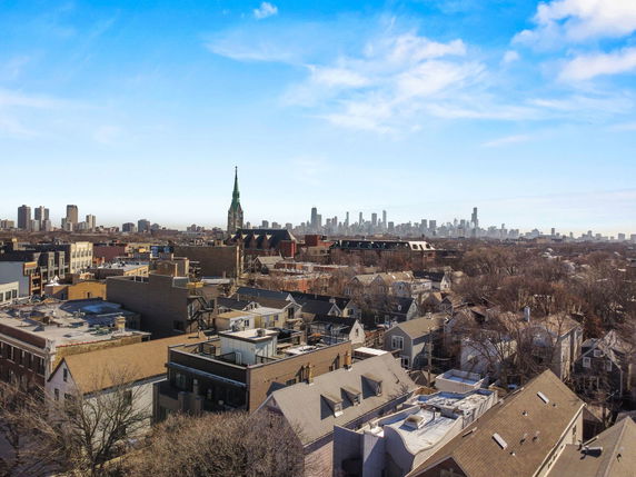 Panoramic view of a cityscape with buildings and a distant skyline under a blue sky.