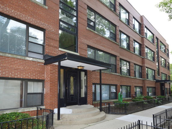 Front view of a multi-story brick building with large windows and entrance with stairs.