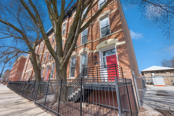 Front view of a multi-story brick townhouse with a red door and metal railing.