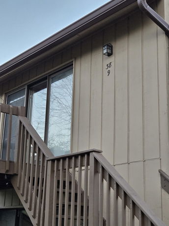 Front view of a building with a wooden staircase and sliding glass door.