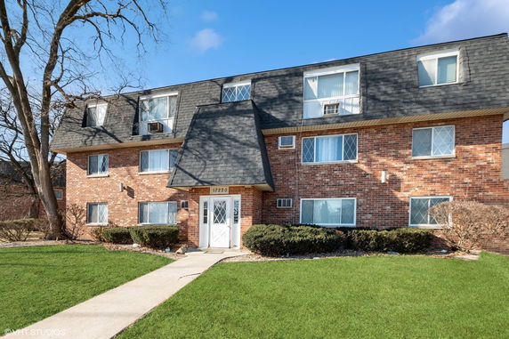 Front view of a brick apartment building with multiple windows and a shingled roof.