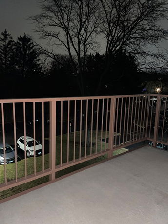 Nighttime view from a balcony showing a parking area and trees.
