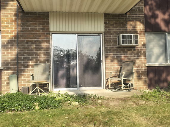 Exterior view of a brick building with sliding glass doors and an air conditioning unit.