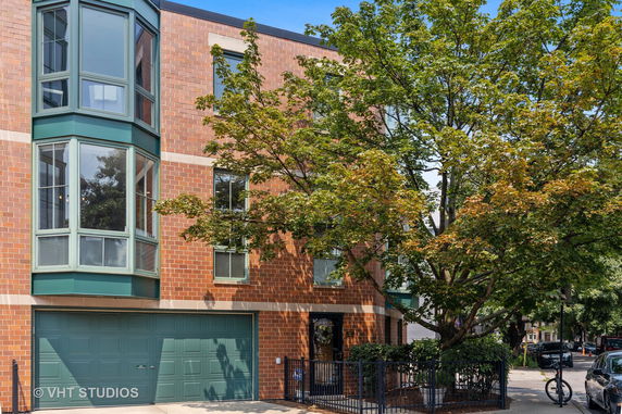 Front view of a multi-story brick townhouse with large bay windows and a green garage door.