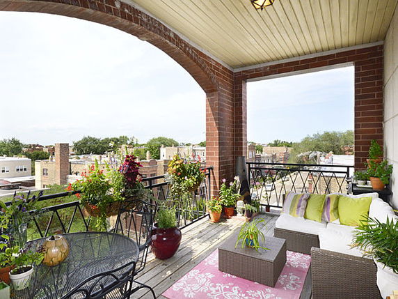Balcony with seating area and potted plants overlooking surrounding neighborhood.