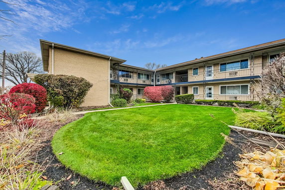 Front view of a two-story apartment building with balconies and a landscaped garden.