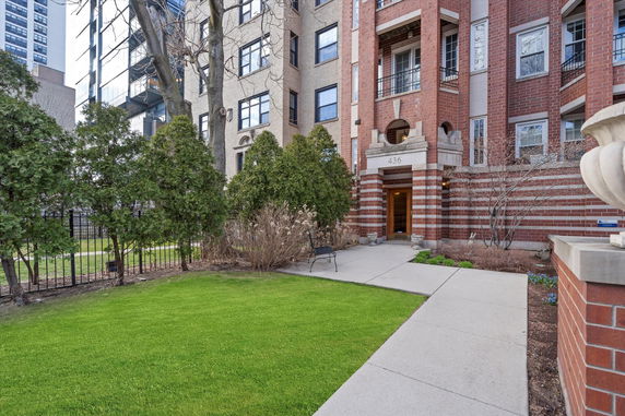 Front view of a multi-story brick building with an entrance and surrounding garden.