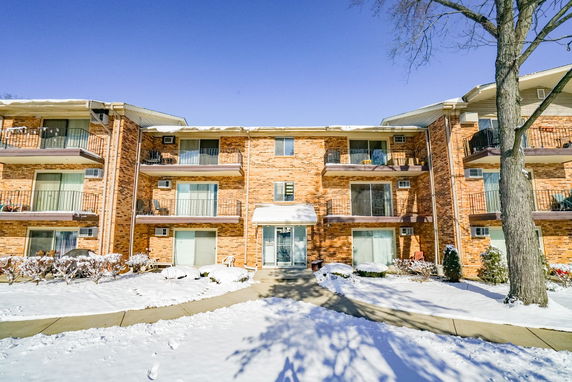 Front view of a multi-story brick apartment building with balconies and snow-covered ground.