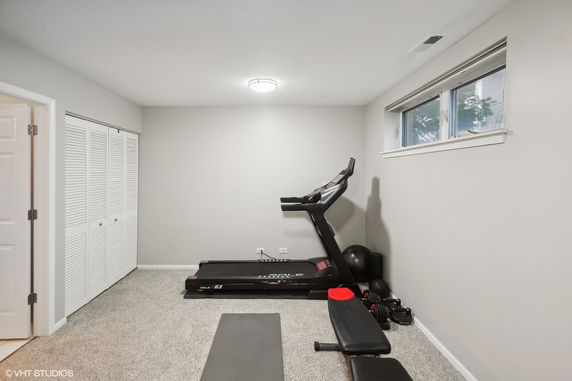 Room with exercise equipment including a treadmill and weights.