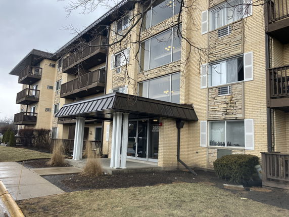 Front view of a multi-story apartment building with balconies and a canopy entrance.
